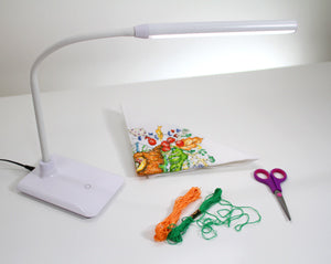 White daylight UNO LED Desk Flex Lamp shown turned on, illuminating crafting materials. 